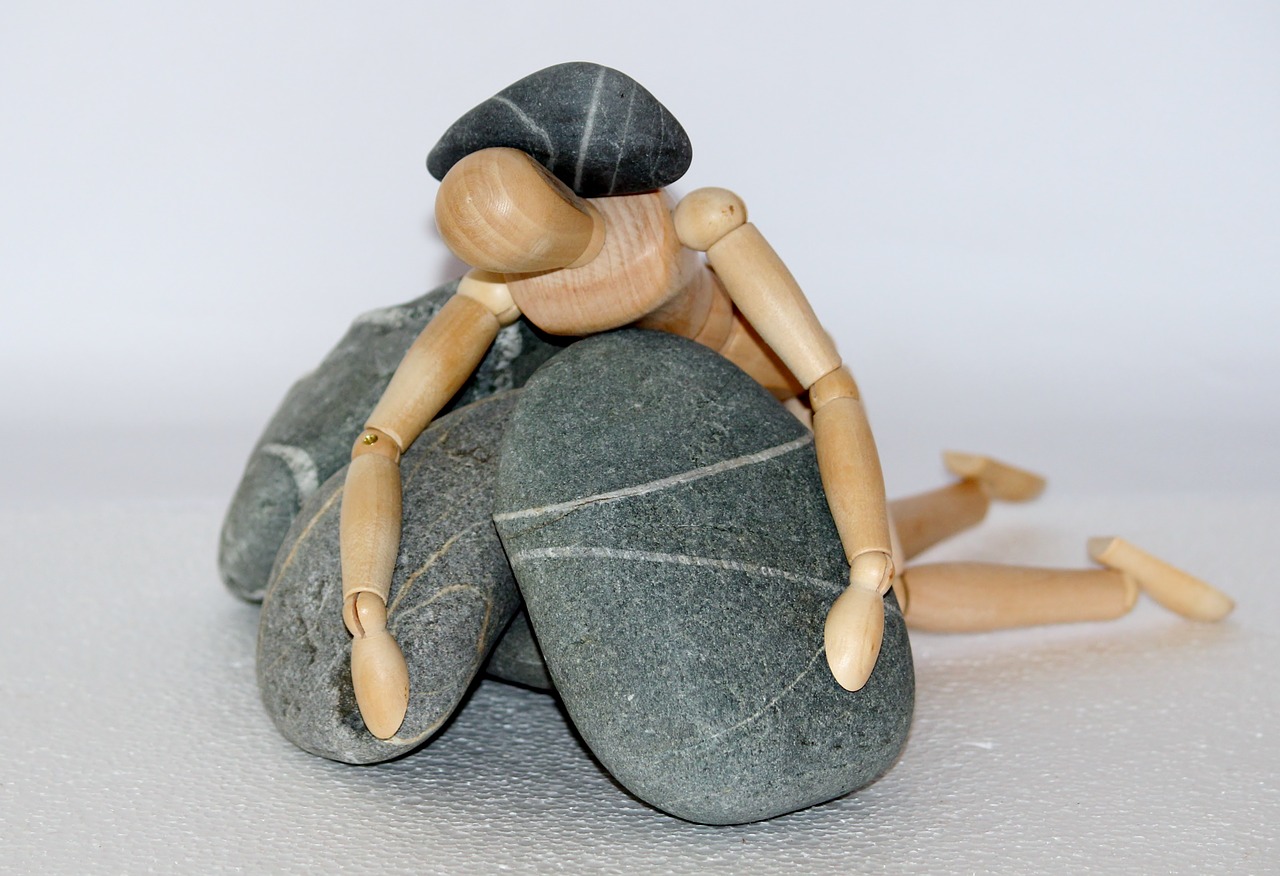 Muñeco articulado encima de varias piedras y con una de ellas sobre la espalda
